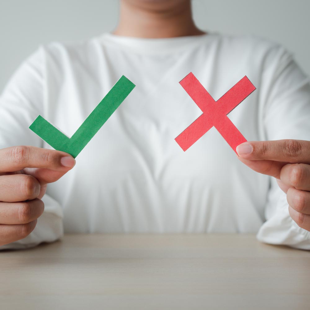 Person hält grünes Häkchen und rotes Kreuz – Symbol für Entscheidungshilfe bei der Wahl vom besten Immobilienmakler Frankfurt.